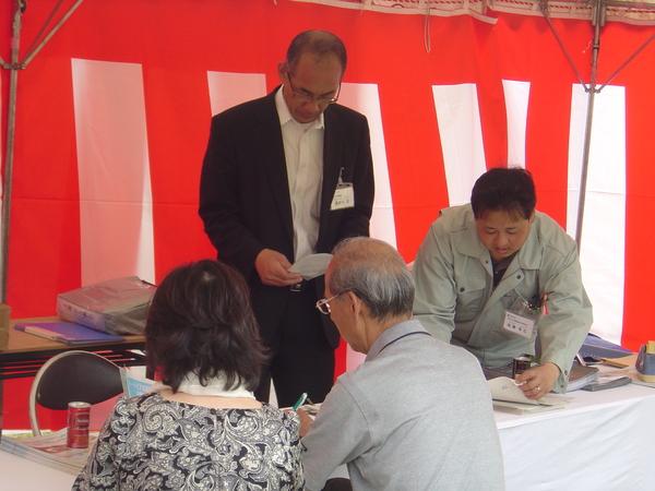 紅白幕が張られたテントの中で椅子に座り手続きをしている年配のご夫婦の写真